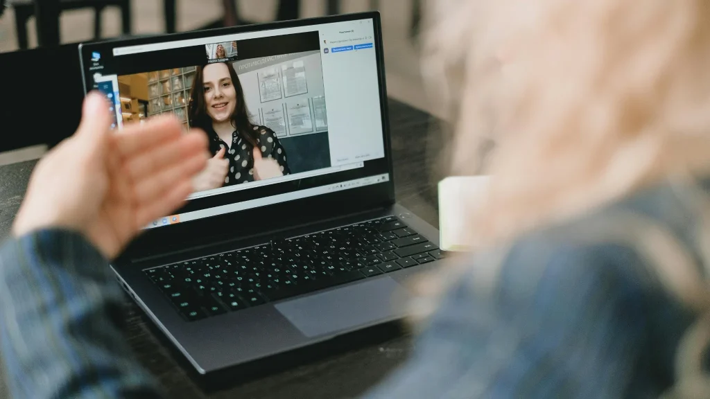 Rozmowa wideo: uśmiechnięta kobieta na ekranie laptopa, przed nim gestykulująca osoba